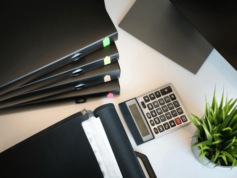 Stack of organized black folders with colored labels next to a calculator, symbolizing thorough claim documentation and intake process management