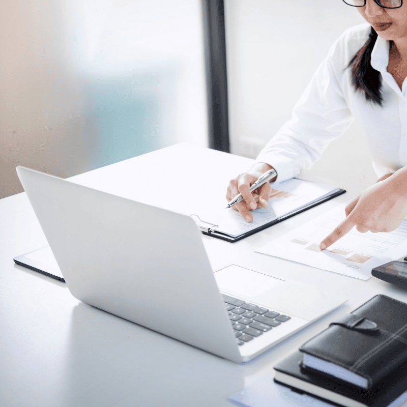 Professional reviewing a printed business guide or SOP document on a desk with a laptop, representing Smart Claims restoration playbooks and systems