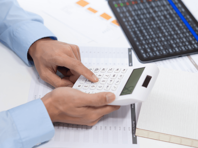 Close-up of a hand using a calculator on financial documents and a tablet, symbolizing accurate Xactimate claims estimating and calculation for submission